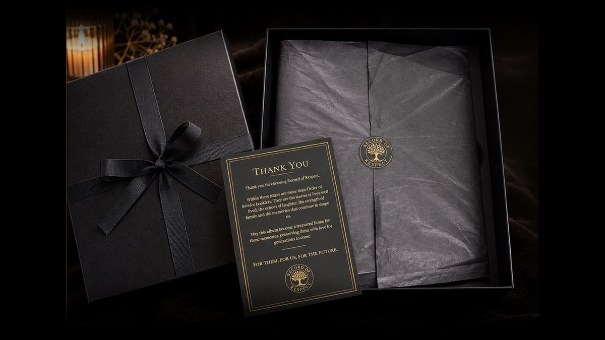 Record of Respect keepsake gift box with black ribbon, opened to reveal the album wrapped in black tissue paper sealed with the gold Record of Respect emblem, beside a gold-bordered thank-you card, lit by candlelight