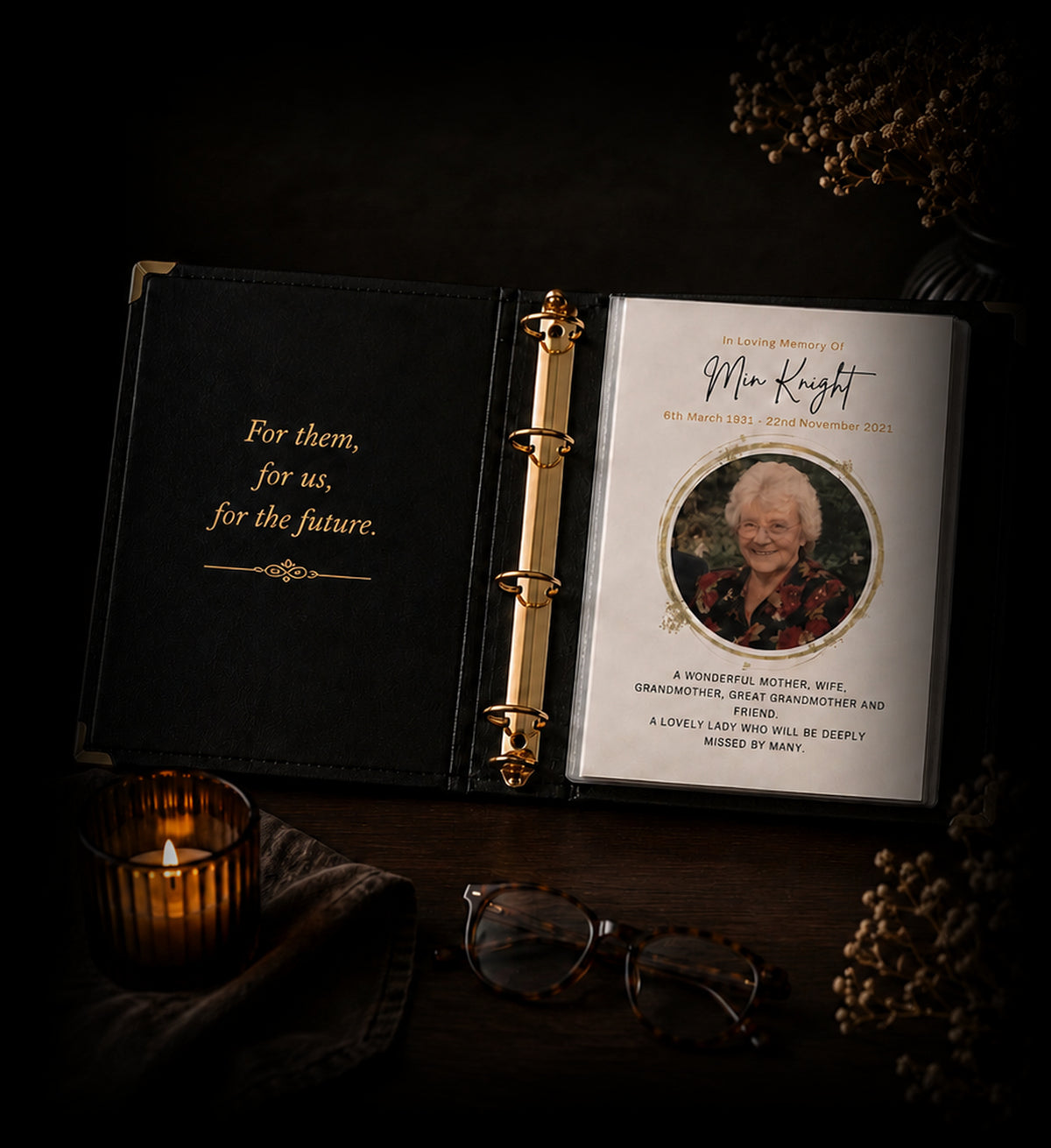 An open Record of Respect album on a dark table, showing a memorial page for Min Knight with her photograph, beside a lit candle, reading glasses and dried flowers